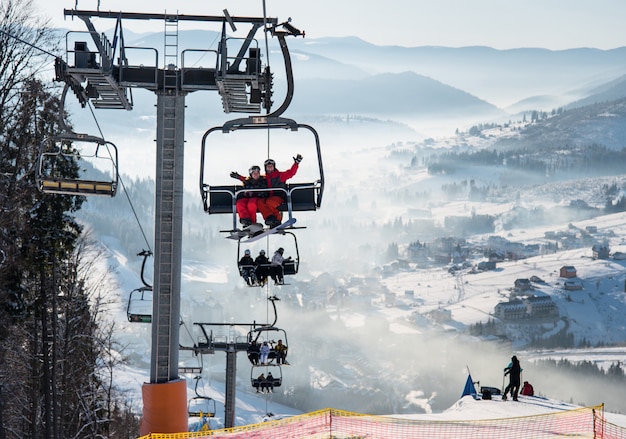 Snowboarders e esquiadores em um teleférico na estância de esqui de inverno com fundo bonito de encostas cobertas de neve, florestas, colinas