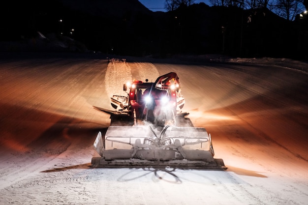 Snowcat ratrack machine haciendo nieve nocturna en la estación de esquí