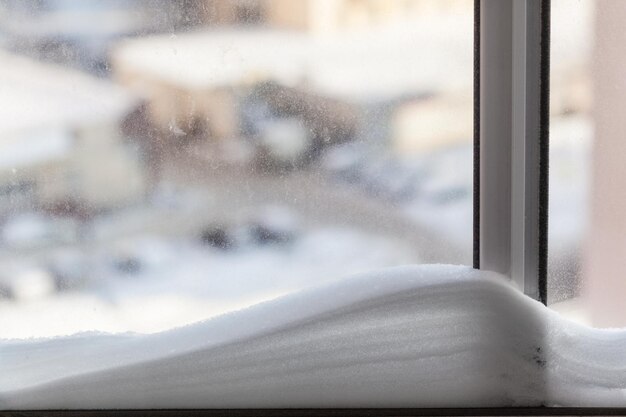 Snowdrift na vidraça de casa e paisagem urbana