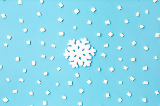 Snowlake criativo sob marshmallow branco sobre fundo azul claro.