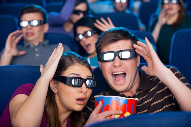 So realistischer Film! Geschockte junge Leute in dreidimensionaler Brille gestikulieren beim gemeinsamen Filmschauen im Kino