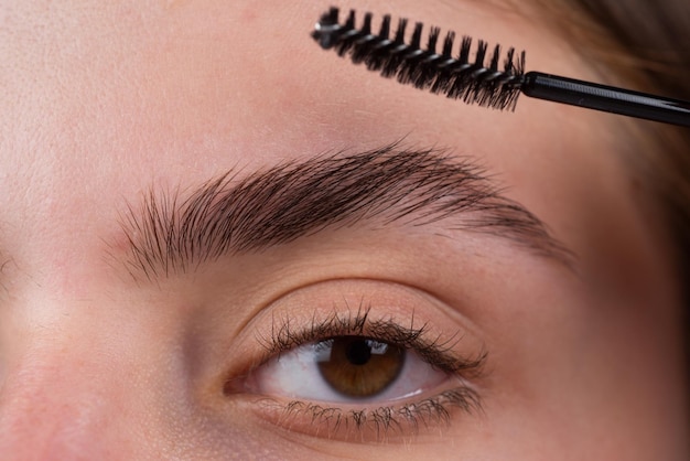 Sobrancelhas da mulher Linda garota com pincel de sobrancelha Garota com maquiagem natural Correção de sobrancelha Macro close-up de sobrancelhas Microblading modelagem de sobrancelhas