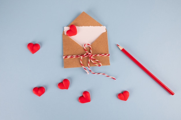 Sobre artesanal con tarjeta blanca en blanco, avión de papel y corazones en la mesa azul