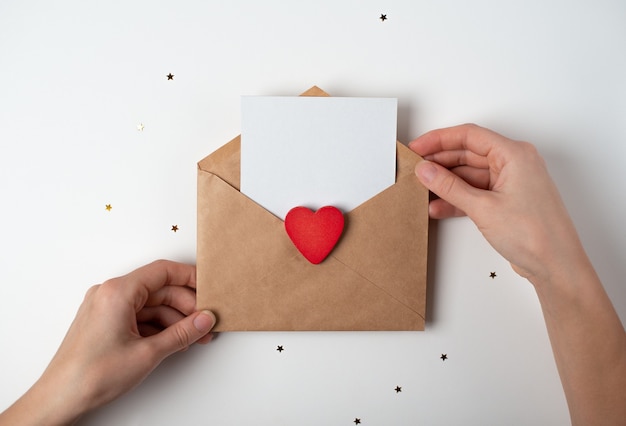 Sobre de artesanía con un corazón rojo y una hoja de papel en blanco dentro en manos de la mujer. Concepto de San Valentín.