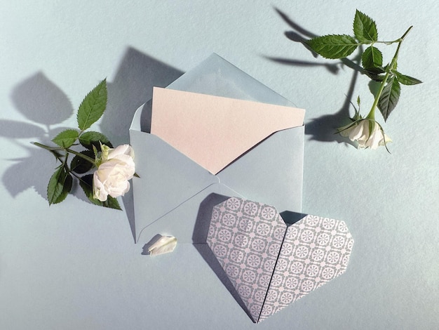Sobre azul claro con tarjeta en blanco rosas blancas y corazón de papel decorativo en fondo pastel perfecto para ocasiones románticas