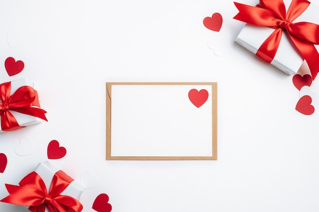 Sobre de cajas de regalo con tarjeta en blanco y corazones rojos sobre blanco