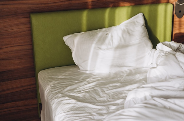 Foto sobre una cama en el dormitorio caen los rayos del sol. cómoda cama con sábanas blancas en casa