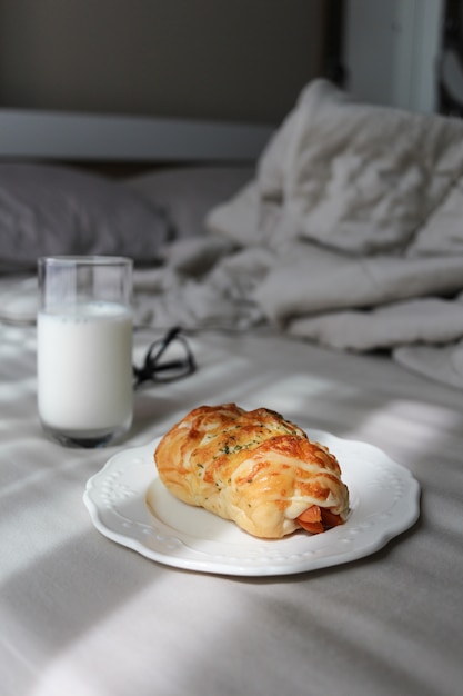 Foto sobre la cama hay un plato de rollo de salchicha con leche. desayuno en concepto de cama.