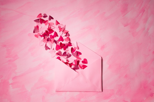 Sobre con corazones de papel sobre fondo rosa. Los corazones despegan del interior del sobre abierto. Carta de amor romántica.