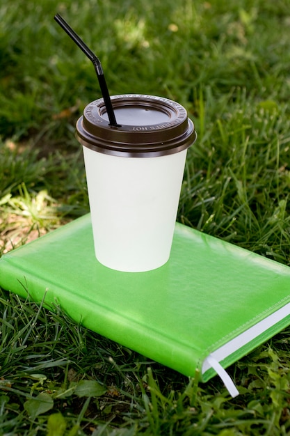 Sobre un cuaderno verde hay una taza de papel blanco con una barra de café o té negro caliente.