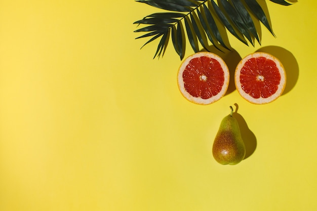 sobre un fondo amarillo se encuentra una rama de palmera, una toronja y una pera cortadas en dos.