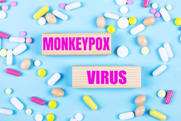 Sobre un fondo azul claro píldoras multicolores y bloques de madera con el texto MONKEYPOX VIRUS Pharmaceutics Medical concept