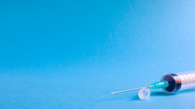 Foto sobre un fondo azul se encuentra una jeringa médica con una aguja. epidemia. copiar el espacio el concepto de recolección de sangre y vacunas inyectables, equipo médico para inyección hipodérmica, tema de atención médica.