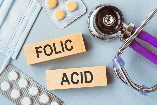 Sobre un fondo azul un estetoscopio y un bloque de madera con la palabra ÁCIDO FÓLICO Concepto médico