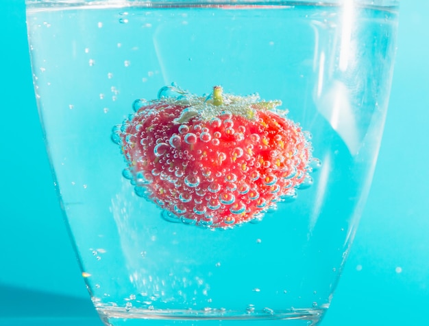 Foto sobre un fondo azul fresas en un vaso con burbujas.