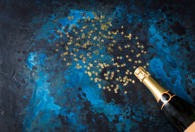 sobre un fondo azul oscuro una botella de champaña y estrellas doradas