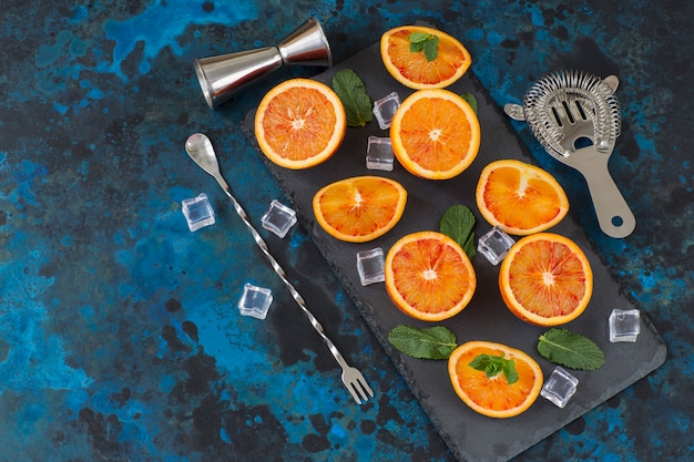 Sobre un fondo azul oscuro, cortar en trozos naranjas, hielo, artículos para la preparación de un cóctel.