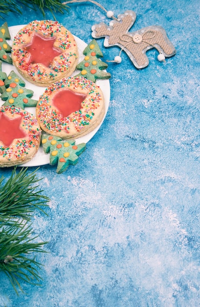 Sobre un fondo azul, un plato con galletas navideñas hechas a mano, ramas de pino y una decoración navideña