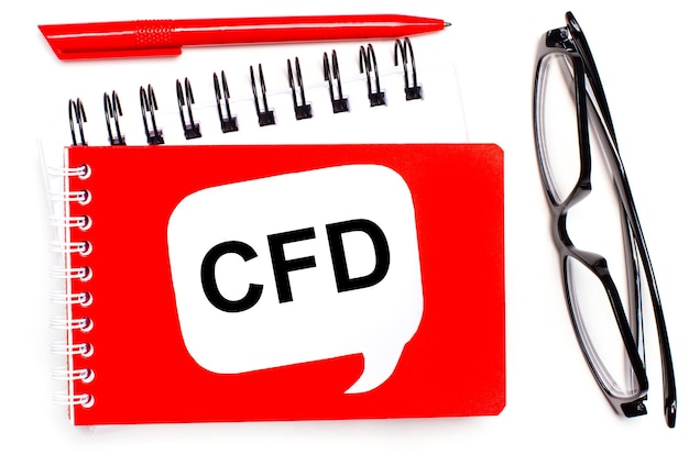 Sobre un fondo blanco, libretas blancas y rojas, gafas negras, un bolígrafo rojo y una tarjeta blanca con el texto Contrato CFD por diferencia
