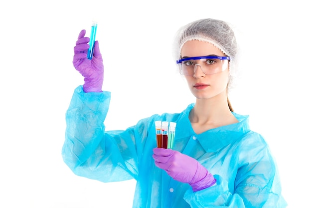 Sobre un fondo blanco, la mujer con una capa protectora con diferentes tubos con un poco de líquido en la mano muestra uno que es azul de ellos.