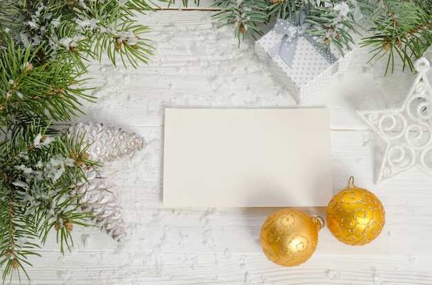 Sobre un fondo blanco: una tarjeta blanca, un regalo y dos bolas de oro. Decoración de año nuevo.