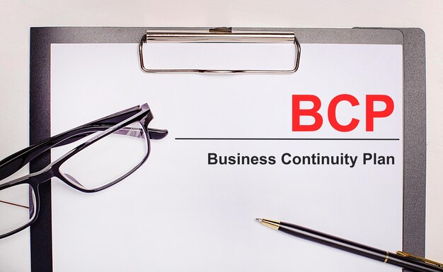 Sobre un fondo de madera clara, anteojos, un bolígrafo y una hoja de papel con el texto BCP Business Continuity Plan Business concept