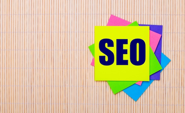 Sobre un fondo de madera clara, pegatinas multicolores brillantes con el texto SEO Search Engine Optimization