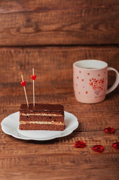 Sobre un fondo de madera, un postre festivo con té, un trozo de tarta en un plato con corazones