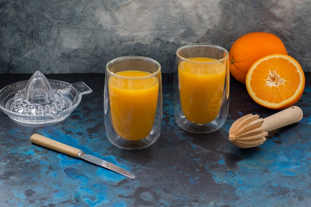 Sobre un fondo oscuro, dos vasos con jugo de naranja.