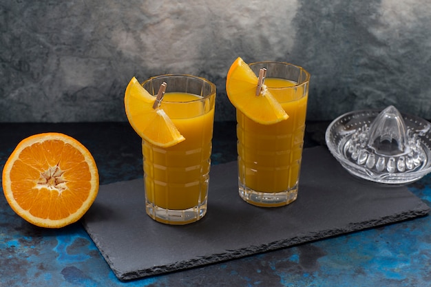 Sobre un fondo oscuro, dos vasos con jugo de naranja.