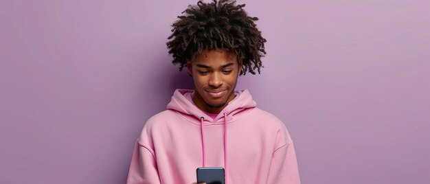 Sobre un fondo púrpura claro un joven afroamericano feliz y rizado sostiene un teléfono celular y envía mensajes de texto en un teléfono inteligente usando aplicaciones digitales móviles