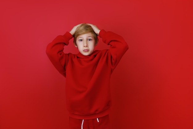 Sobre un fondo rojo se encuentra un niño vestido con un traje rojo que se agarró la cabeza con miedo