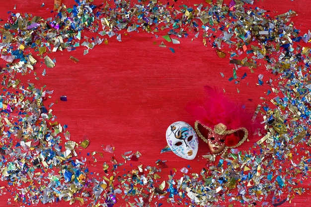 Sobre un fondo rojo hay dos máscaras de carnaval y confeti de colores alrededor.
