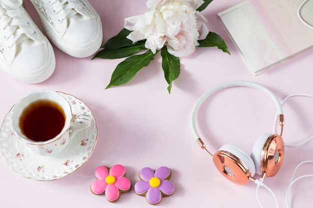 sobre un fondo rosa: auriculares, zapatillas de deporte, peonía, una taza de té