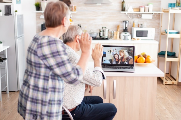 Sobre la foto de los abuelos saludando en la computadora portátil, hablando con la familia sentada en la cocina, comunicándose con su sobrina a través de una videollamada. Padres e hija adulta hablando mediante la aplicación de videoconferencia c