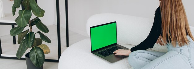 Sobre el hombro de una mujer escribiendo en una computadora portátil con una pantalla keygreen