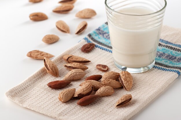 Sobre una mesa blanca, leche de almendras en un vaso con almendras