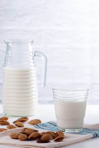 Sobre una mesa blanca, leche de almendras en un vaso con almendras