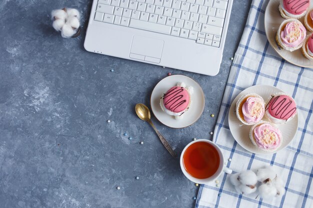 Sobre la mesa gris hay una computadora portátil, un plato de pasteles de crema, una taza de té