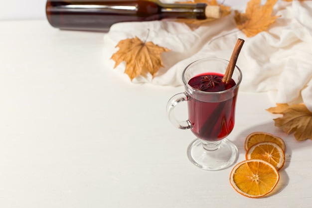 Sobre la mesa había una copa de vino caliente con especias, una botella, un pañuelo, hojas secas y naranjas. Humor de otoño, un método para mantenerse caliente en el frío, copyspace.
