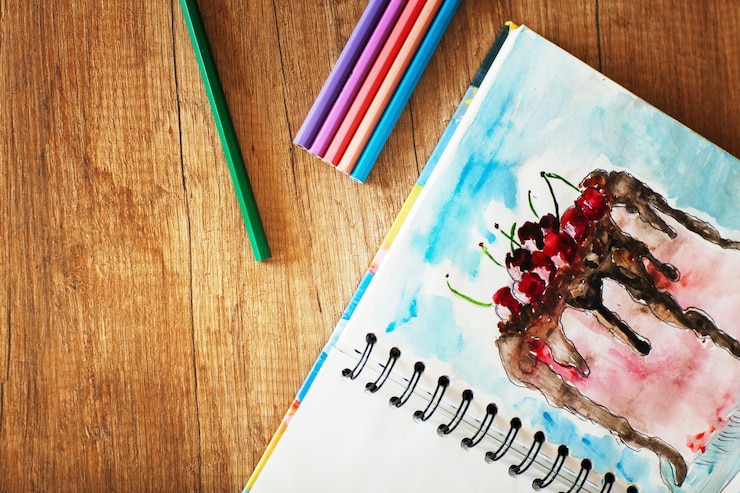 Foto sobre la mesa hay lápices de colores y un dibujo de acuarela de un pastel con cerezas. vista lateral