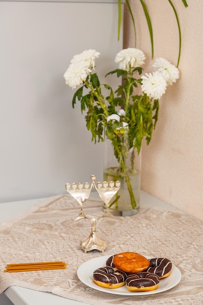 Sobre la mesa hay un plato de donas, velas y Hanukkah y un jarrón de flores preparándose para Hanukkah.