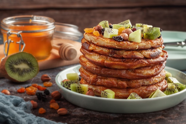 Foto sobre la mesa hay un plato con panqueques, miel, kiwi, nueces y pasas.