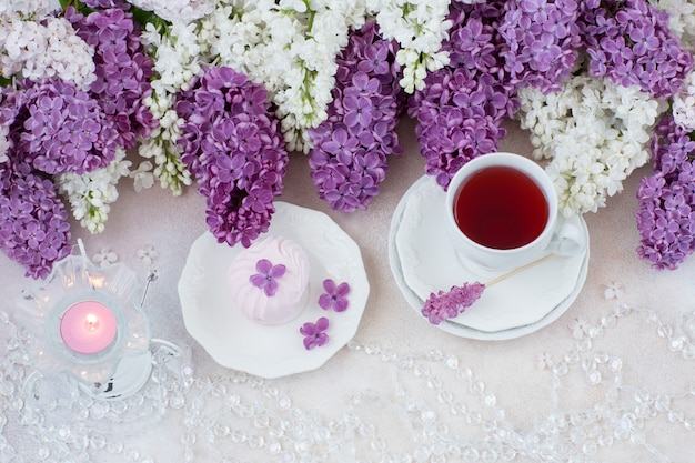 Sobre la mesa hay té y malvaviscos, cuentas, una vela en un candelabro y un ramo de lilas.