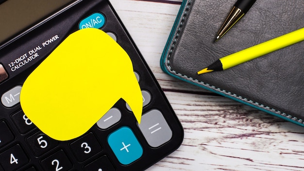 Sobre una mesa de madera clara hay una calculadora, un cuaderno, un bolígrafo, un lápiz amarillo y una tarjeta amarilla con un lugar para insertar texto. Concepto de negocio. Modelo