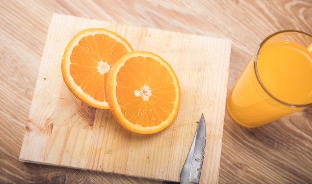 Sobre una mesa de madera un cuchillo, un vaso con una bebida y una naranja