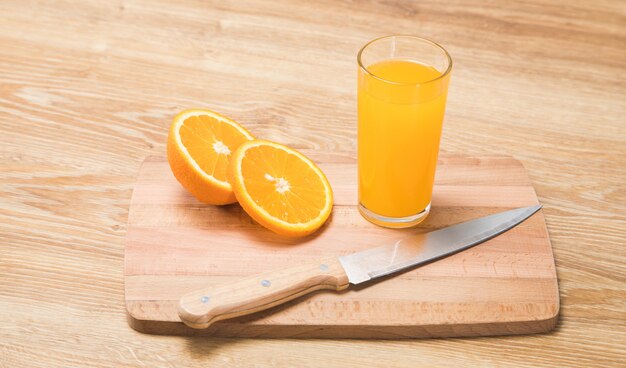 Sobre una mesa de madera un cuchillo, un vaso con una bebida y una naranja