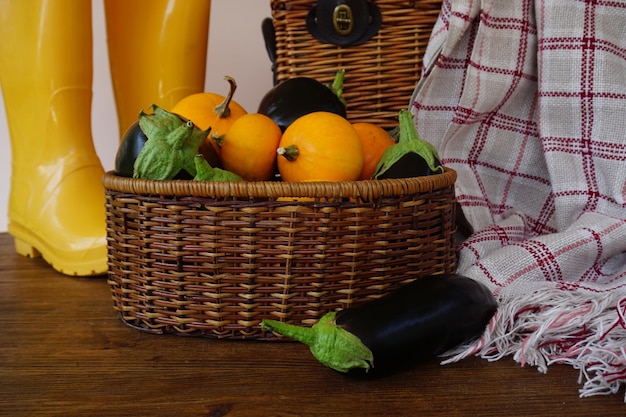 Sobre una mesa de madera hay una cesta de mimbre con una cosecha de berenjenas y calabazas