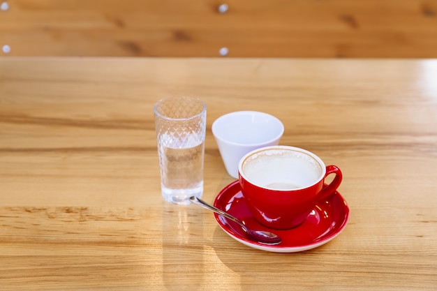 Sobre una mesa de madera hay tazas de café sucias, capuchino y un vaso de agua.