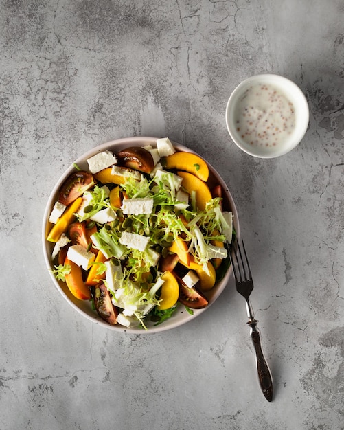 Sobre una mesa de mármol gris hay un plato de ensalada con verduras, nectarina y tomates. Vista superior